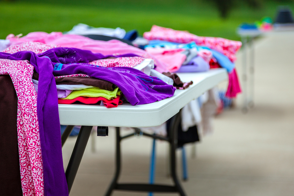 Table of clothing on driveway at a garage sale