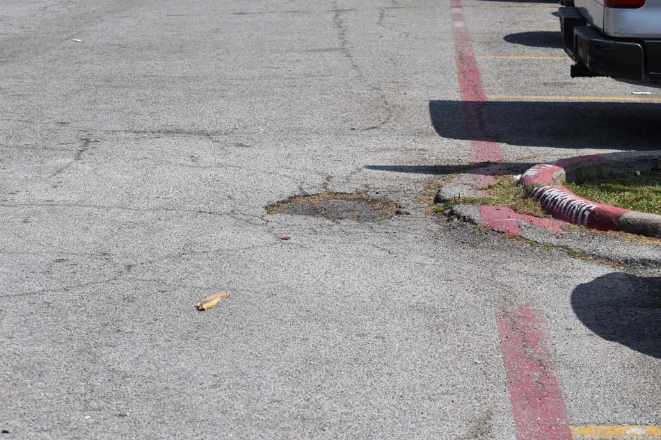 Close-up image of a parking lot with a poorly marked/faded fire lane and a pothole.